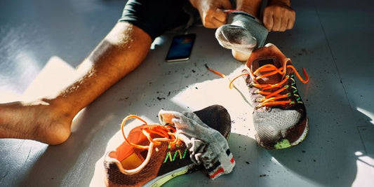 person sitting on the floor with orange tennis shoes beside them removing socks from sweaty feet