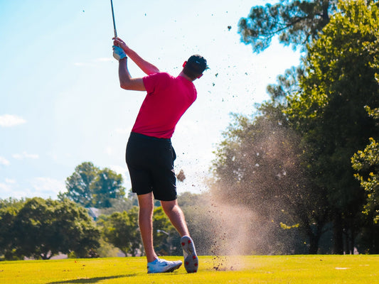 male golf player in red shirt and black shorts swinging a golf club on the course