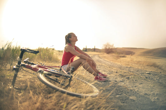 young woman sitting in the grass beside her bicycle to cool off during the summer