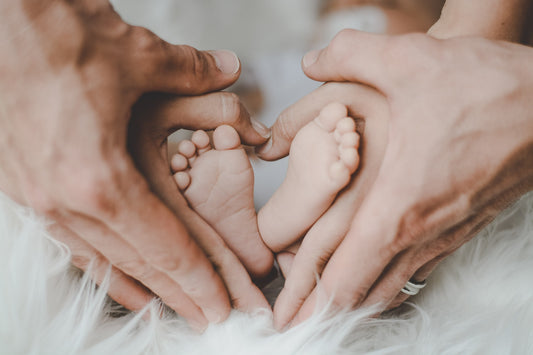 close up of mothers hands around infant feet in the shape of a heart